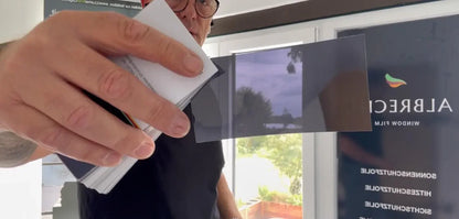Hand hält Muster einer Fensterfolie vor modernem Fenster, Sichtschutz und Sonnenschutz sichtbar