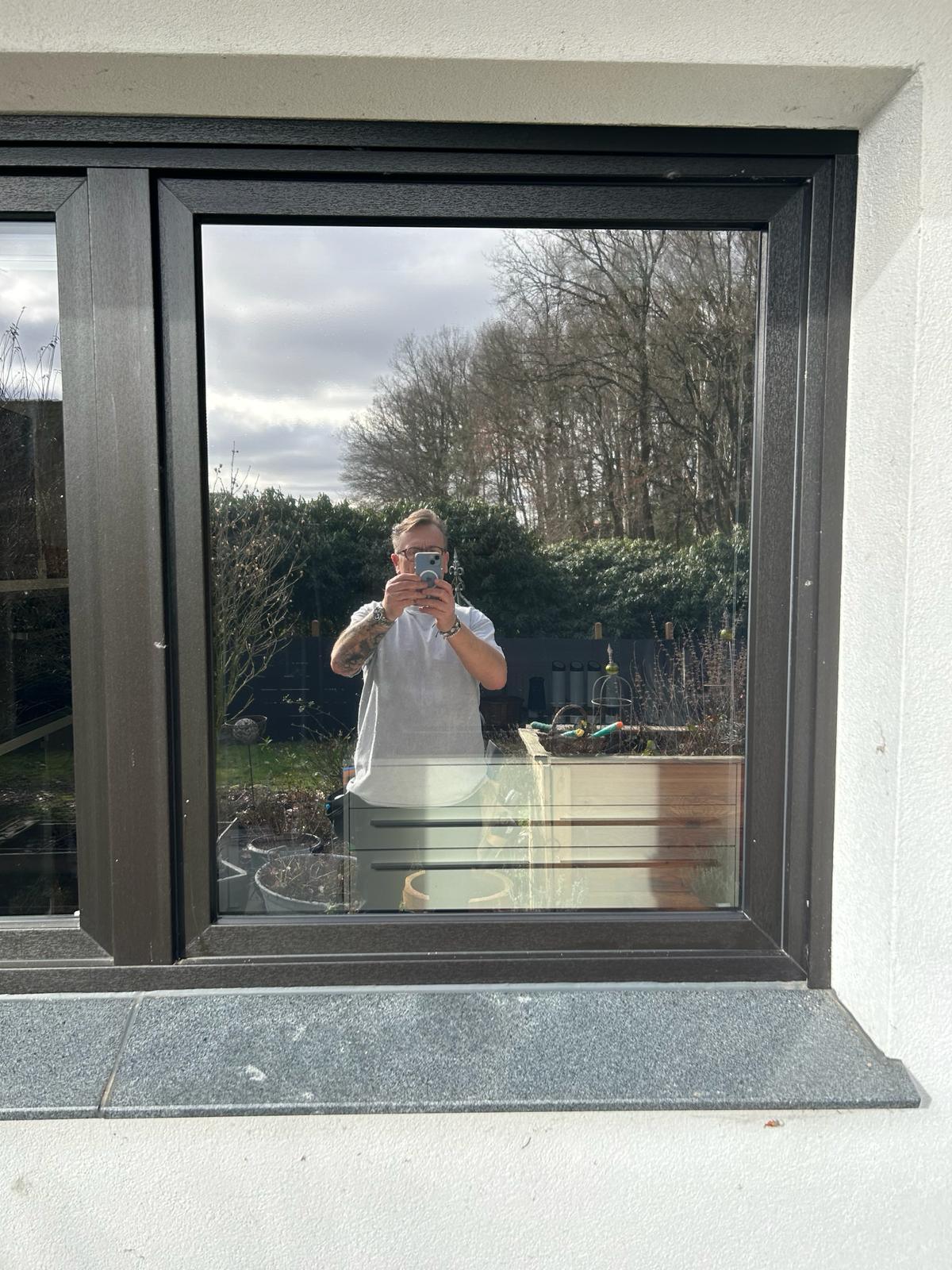 Reflektion eines Mannes in moderner Fensterfolie, Außenansicht, Garten und Bäume im Hintergrund