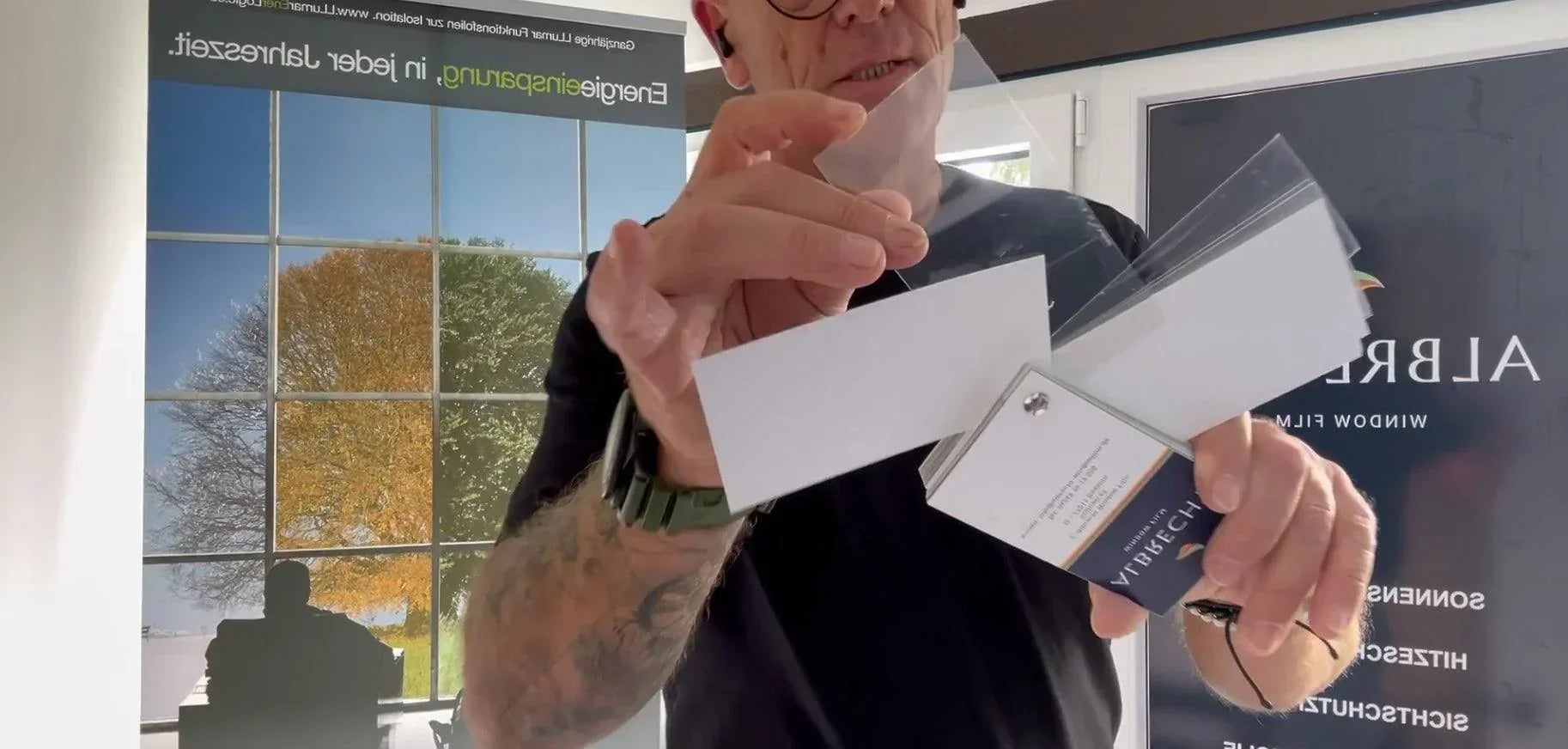 Mann zeigt Musterfächer mit Splitterschutzfolien für Fenster im Innenraum