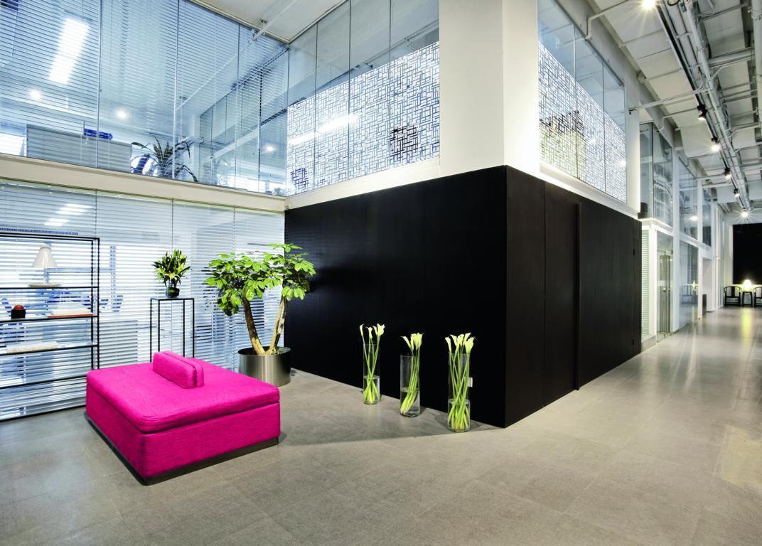 Modernes Büro mit großen Glasflächen, dekorativer Fensterfolie und pinkem Sofa